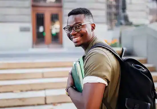 a male college student carrying a backpack and some books