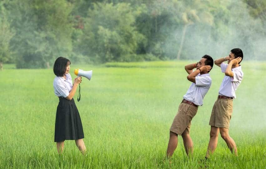 Girl shouting in megaphone at two boys holding their ears