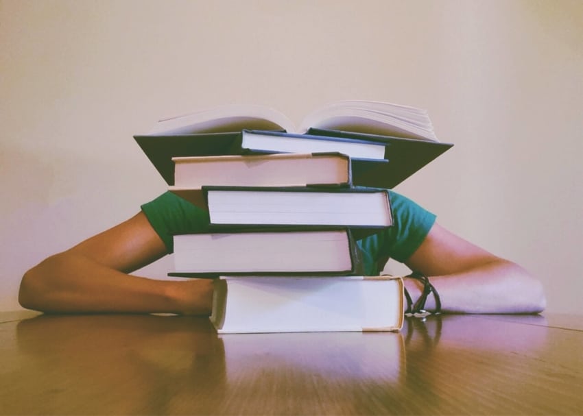 Student with stack of books in a pile