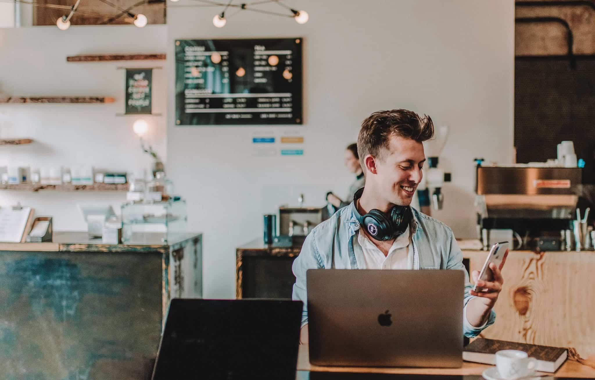 Man studying at a cafe with laptop, phone and book