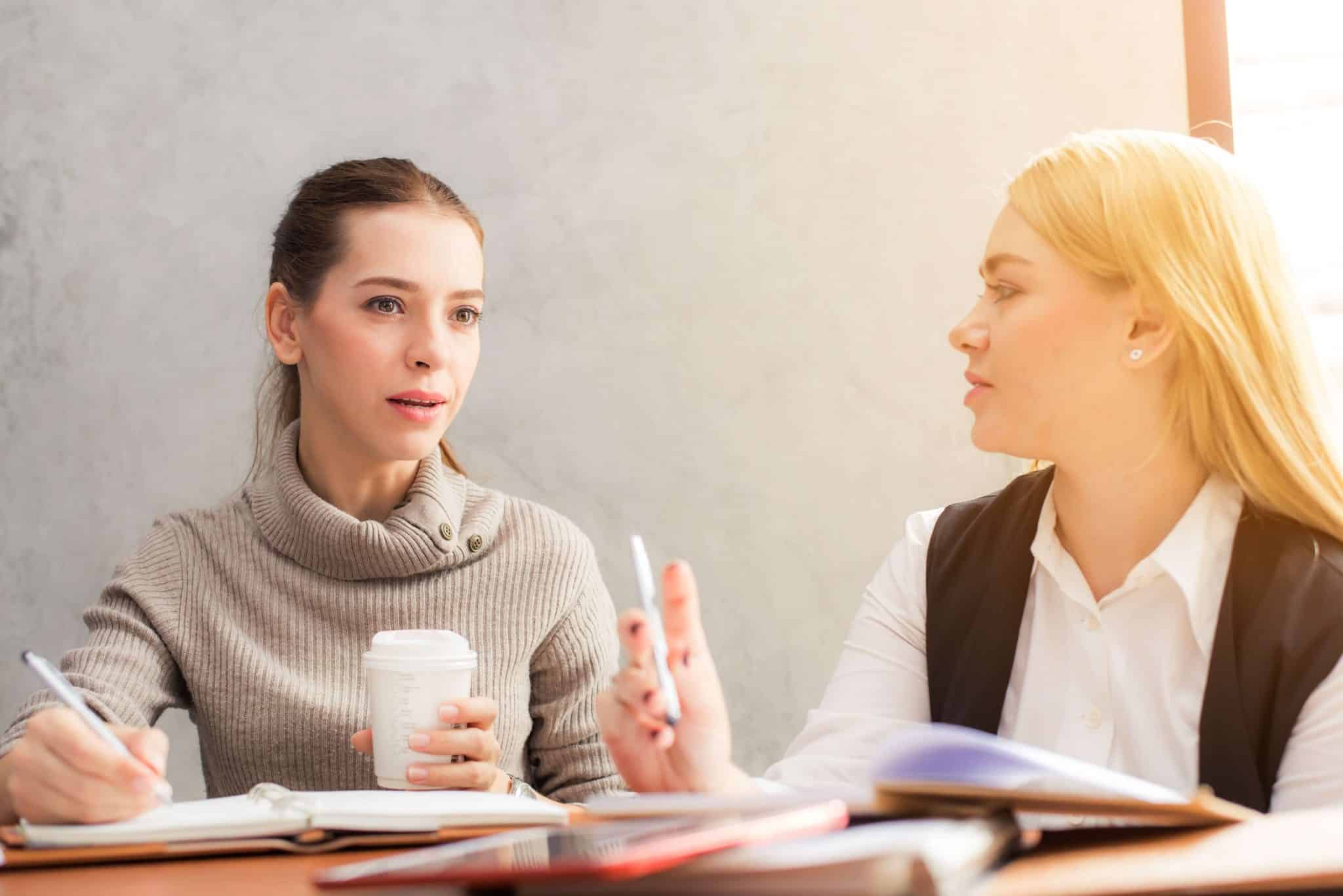 Two women communicating with coffee and notebooks open