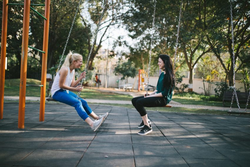 Two girls sitting on swings having a conversation