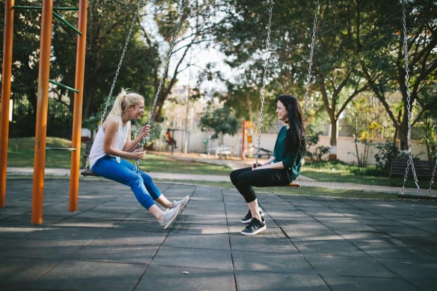 Two girls sitting on swings having a conversation