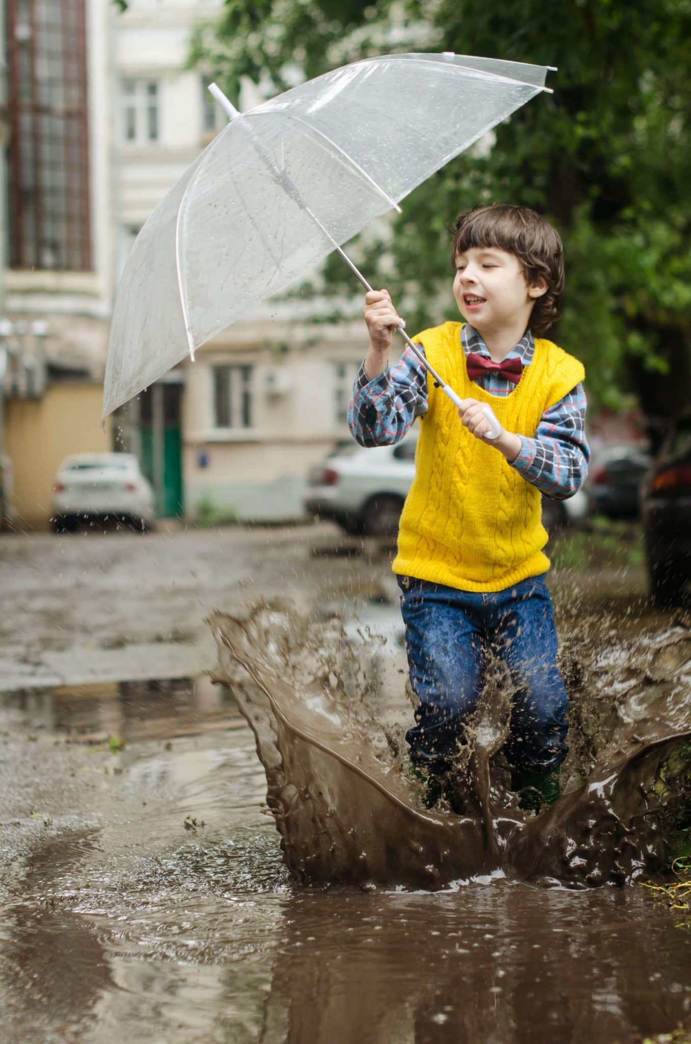 A young boy holding an umbrella and playing around in the rain in between his studies