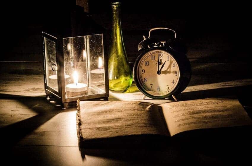 Late night, open book on desk in front of candle, clock, and vase, studying for a minor