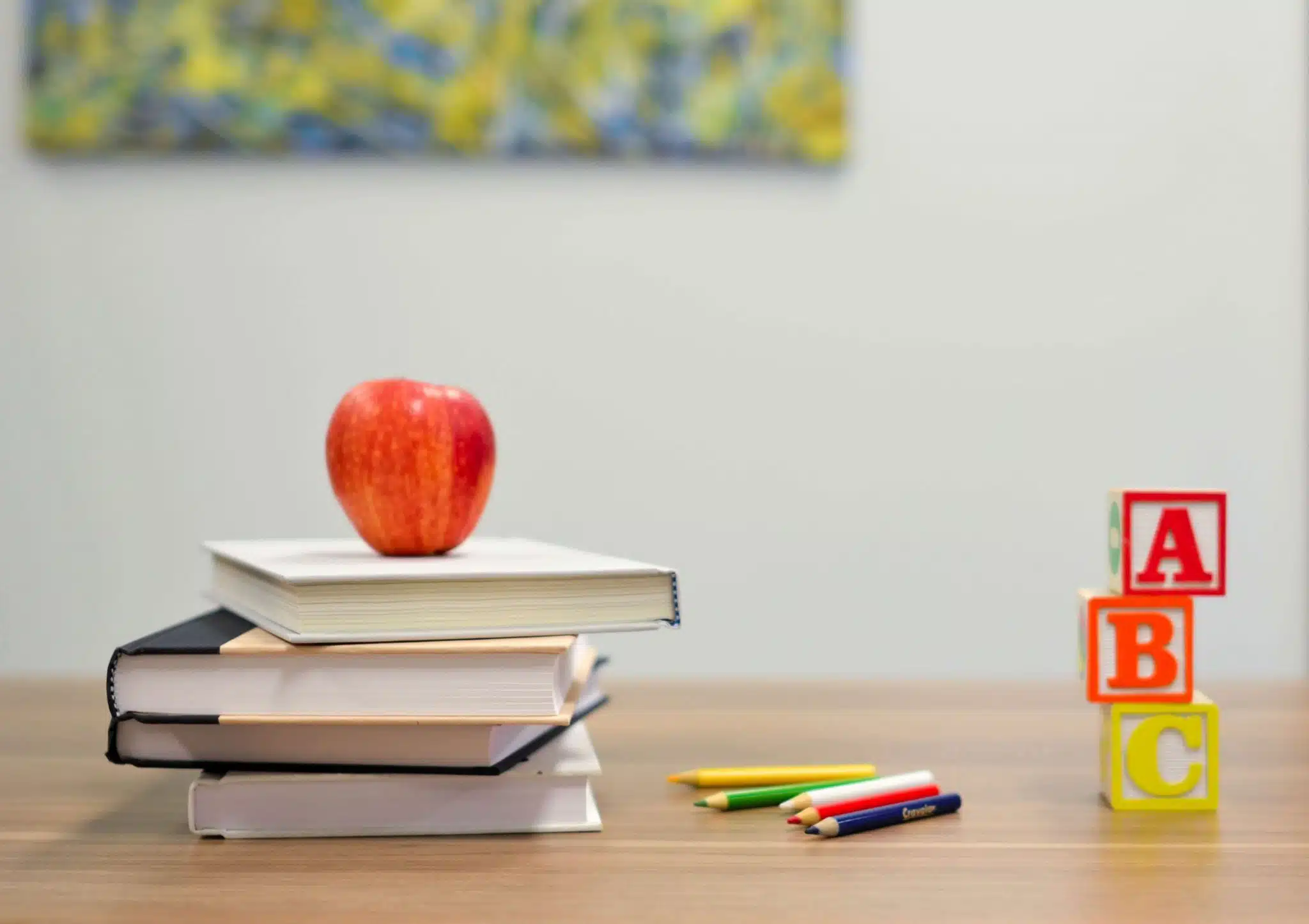 Teacher’s desk with stack of books, blocks, apple, and colored pencils