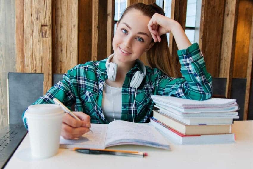 Smiling girl sitting at desk with books and notebooks in front of her