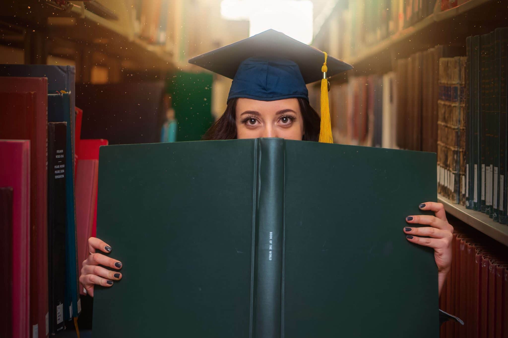 Girl wearing graduation hat in a library with big book