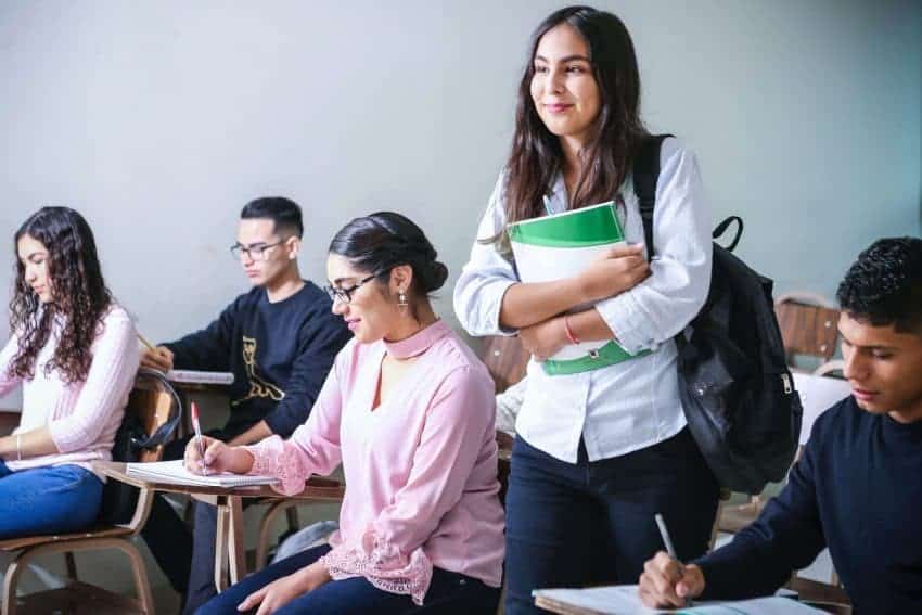 Students in a classroom and girl holding a green notebook