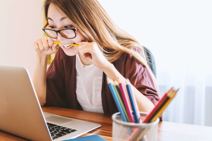 Woman biting a pencil while studying at laptop to avoid failing in college