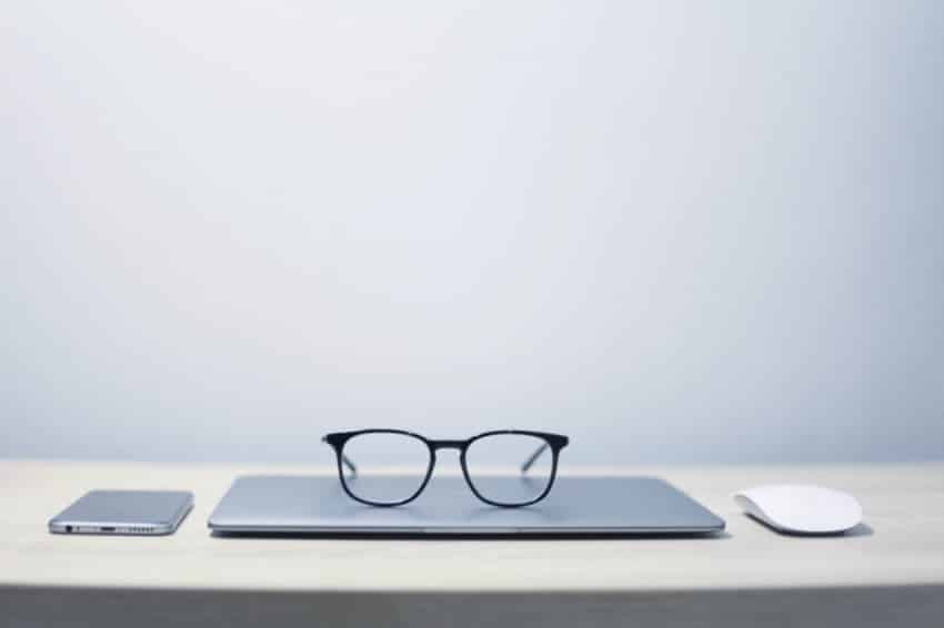 “Black glasses, laptop, phone and mouse at empty desk”