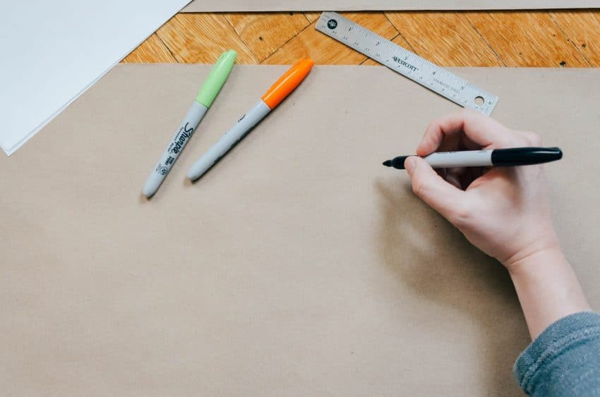 Person writing with sharpies on brown paper