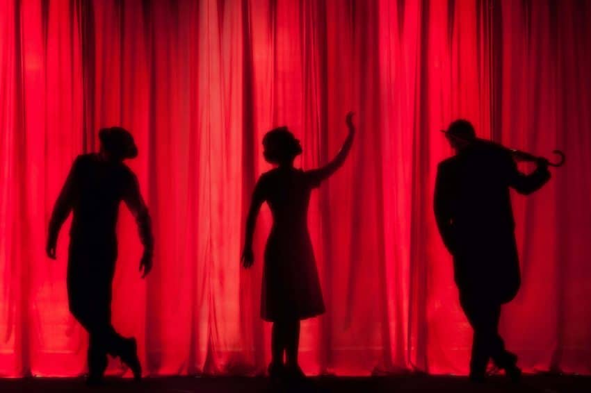 Silhouettes of actors on stage with a red curtain