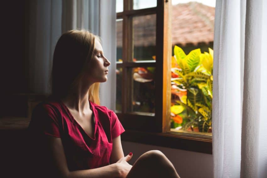 “Woman practicing self-care near a window with plants”