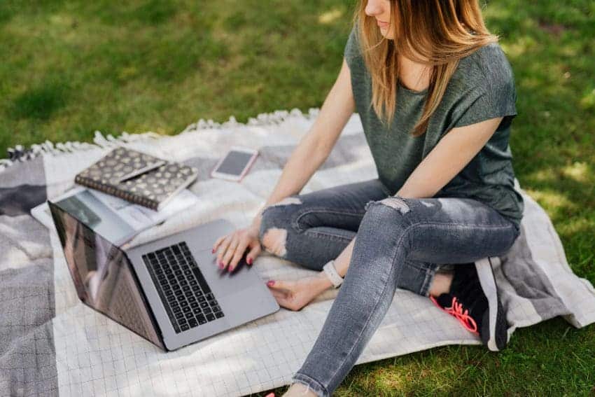 Student sitting on grass with notebook and laptop attending online college