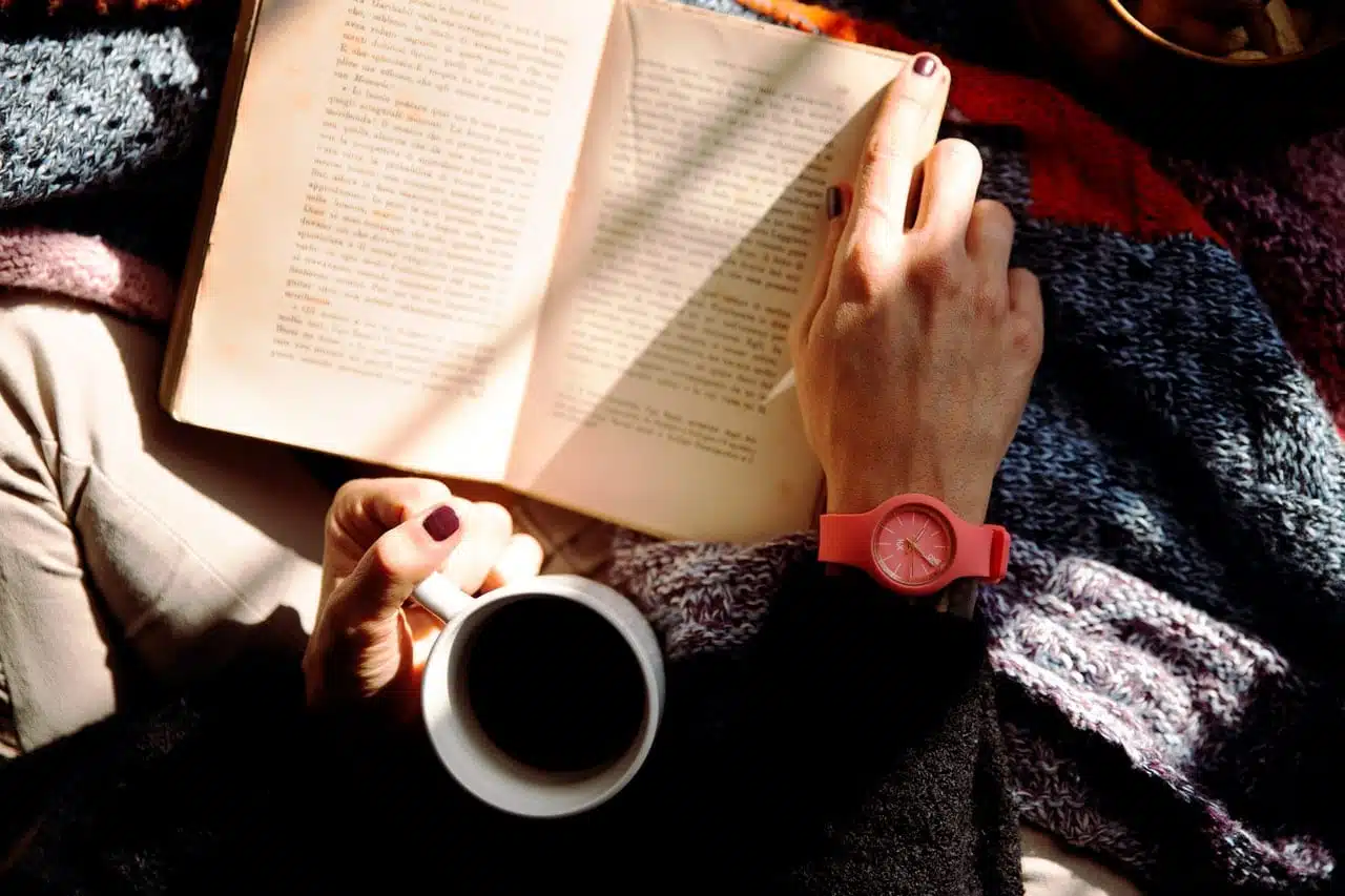 A girl reading a book in bed with a cup of coffee, trying to use her newly acquired reading comprehension skills. 