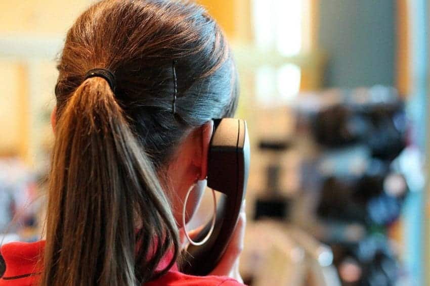 Woman with pony-tail holding landline phone up to her ear