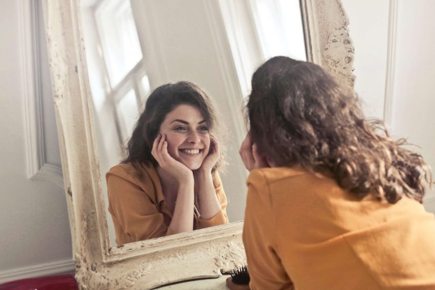 A young woman looking in the mirror and smiling at herself in order to bring happiness to her day.