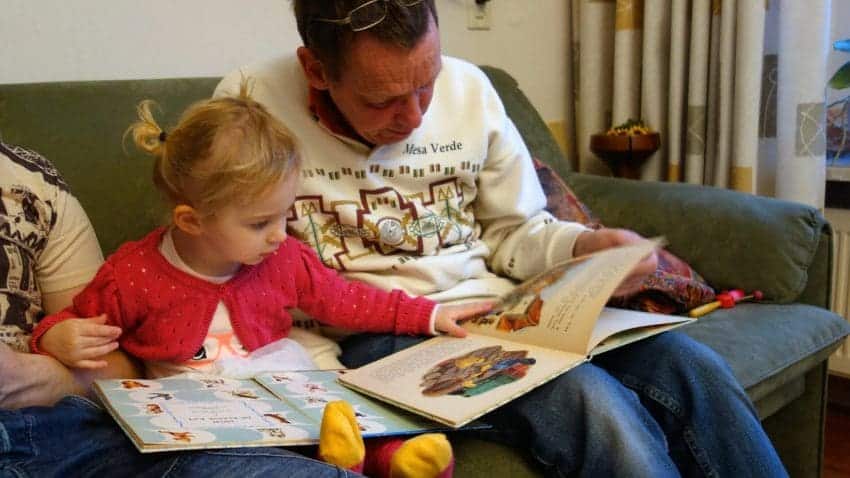 Young child and grandfather reading together on the couch