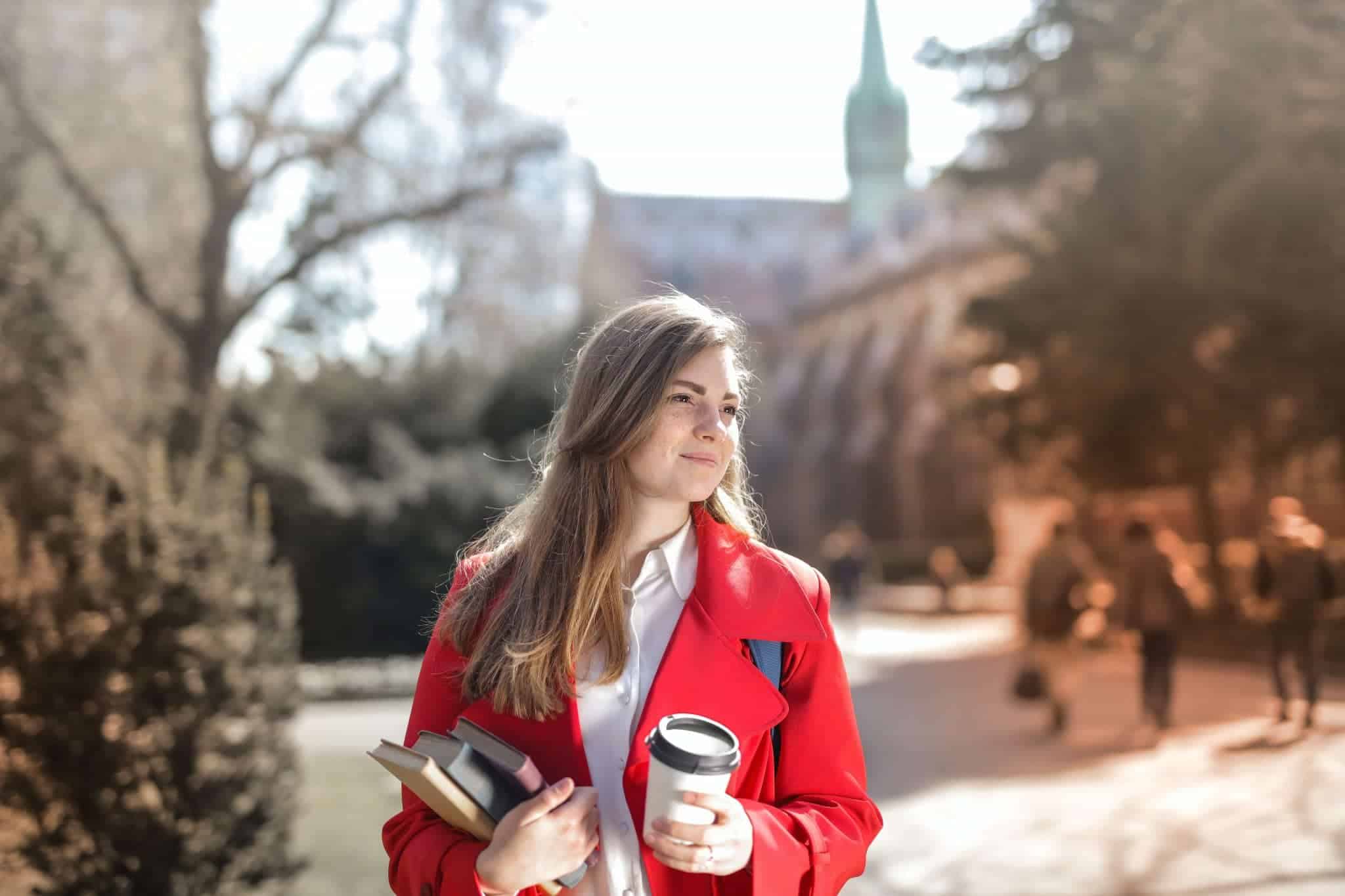 A female college student holding a coffee and some textbooks