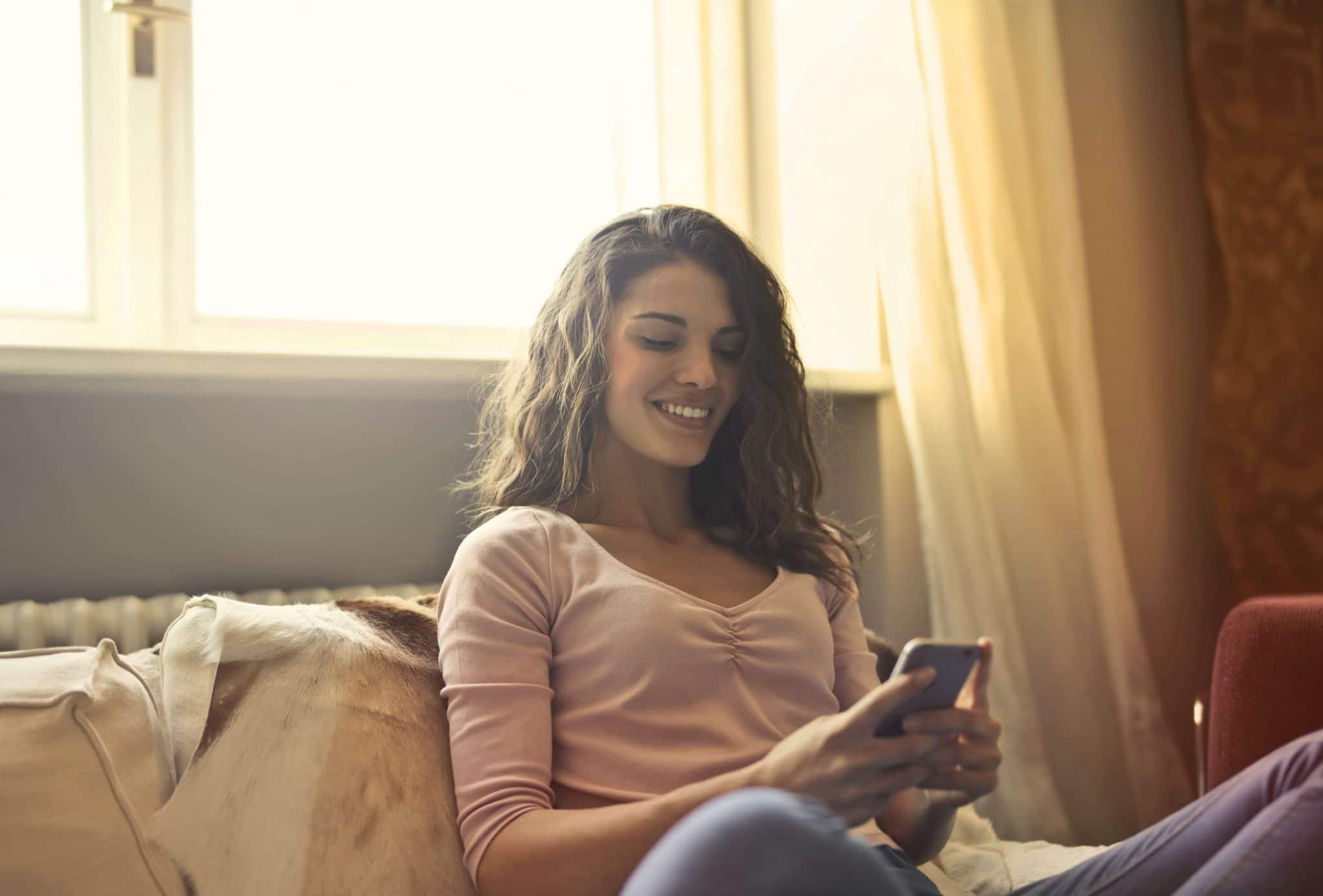 Woman smiling looking at her phone on couch