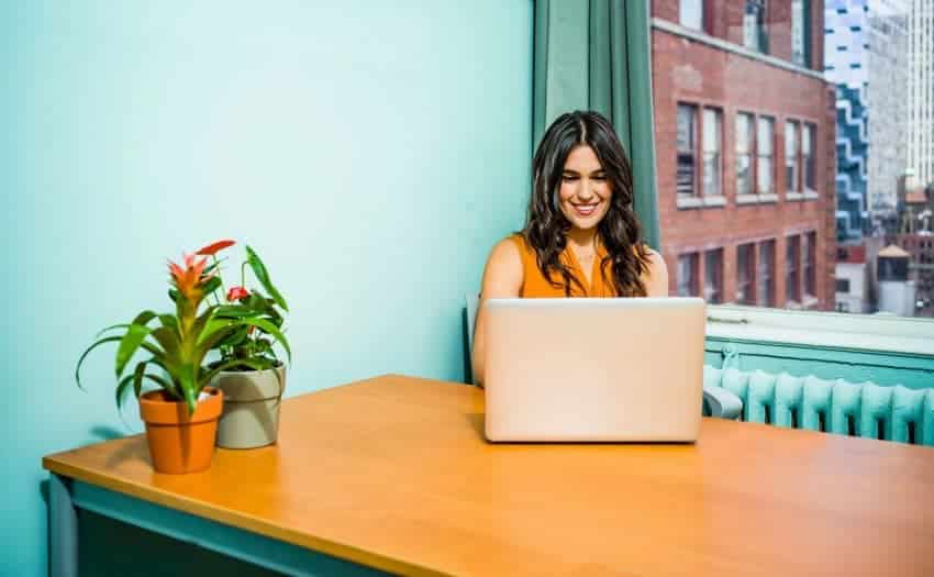 University of the People female student learning online with laptop next to window