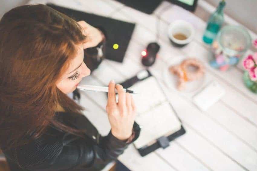 Woman thinking critically over a desk, holding pen to mouth