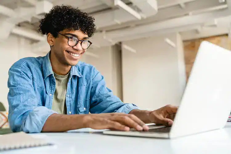 a male college aspirant checking online American colleges' accreditation on his laptop