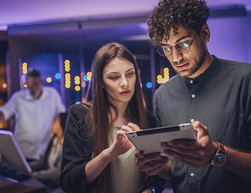 Two students collaborate on a tablet in a modern classroom with soft ambient lighting, focusing on cybersecurity learning and teamwork.