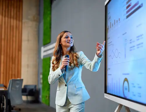 Professional woman presenting data on a large screen with graphs and charts.